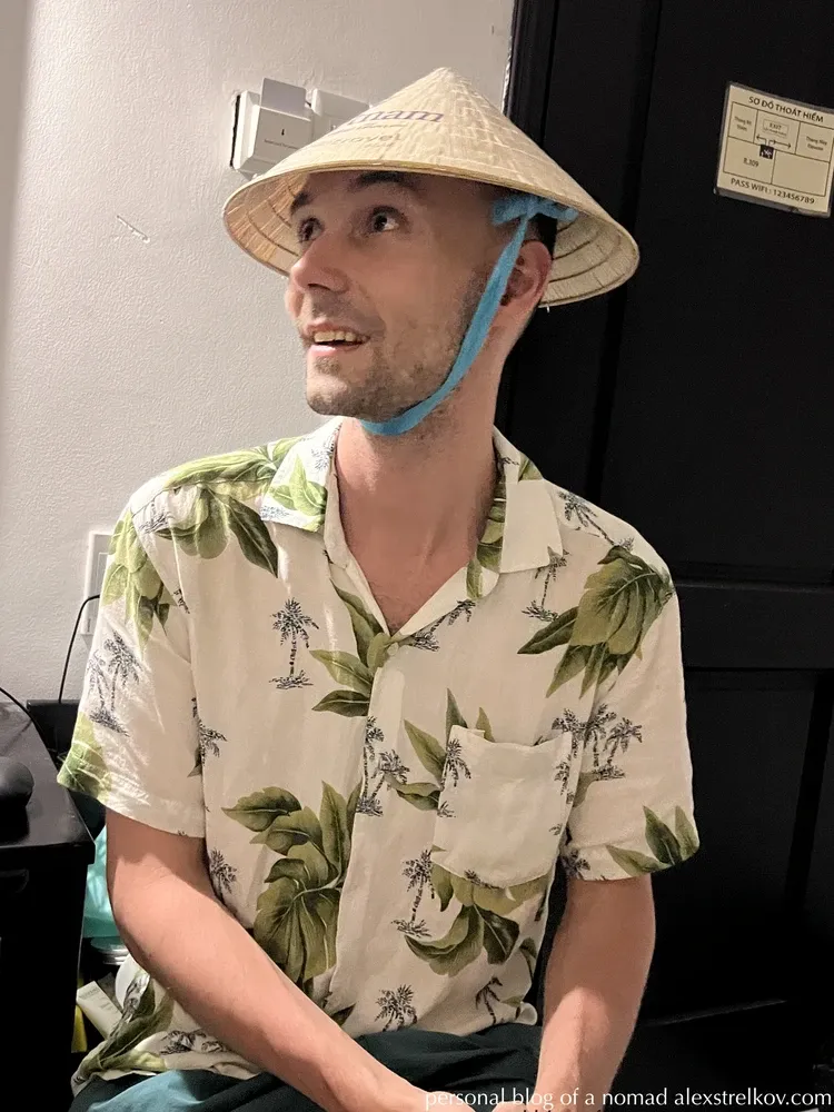 man wearing Vietnamese non la conical hat tropical shirt hotel room 